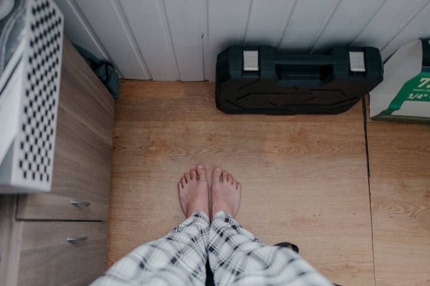 Overhead view of bare feet in pajamas on wooden floor indoors with tool box nearby.