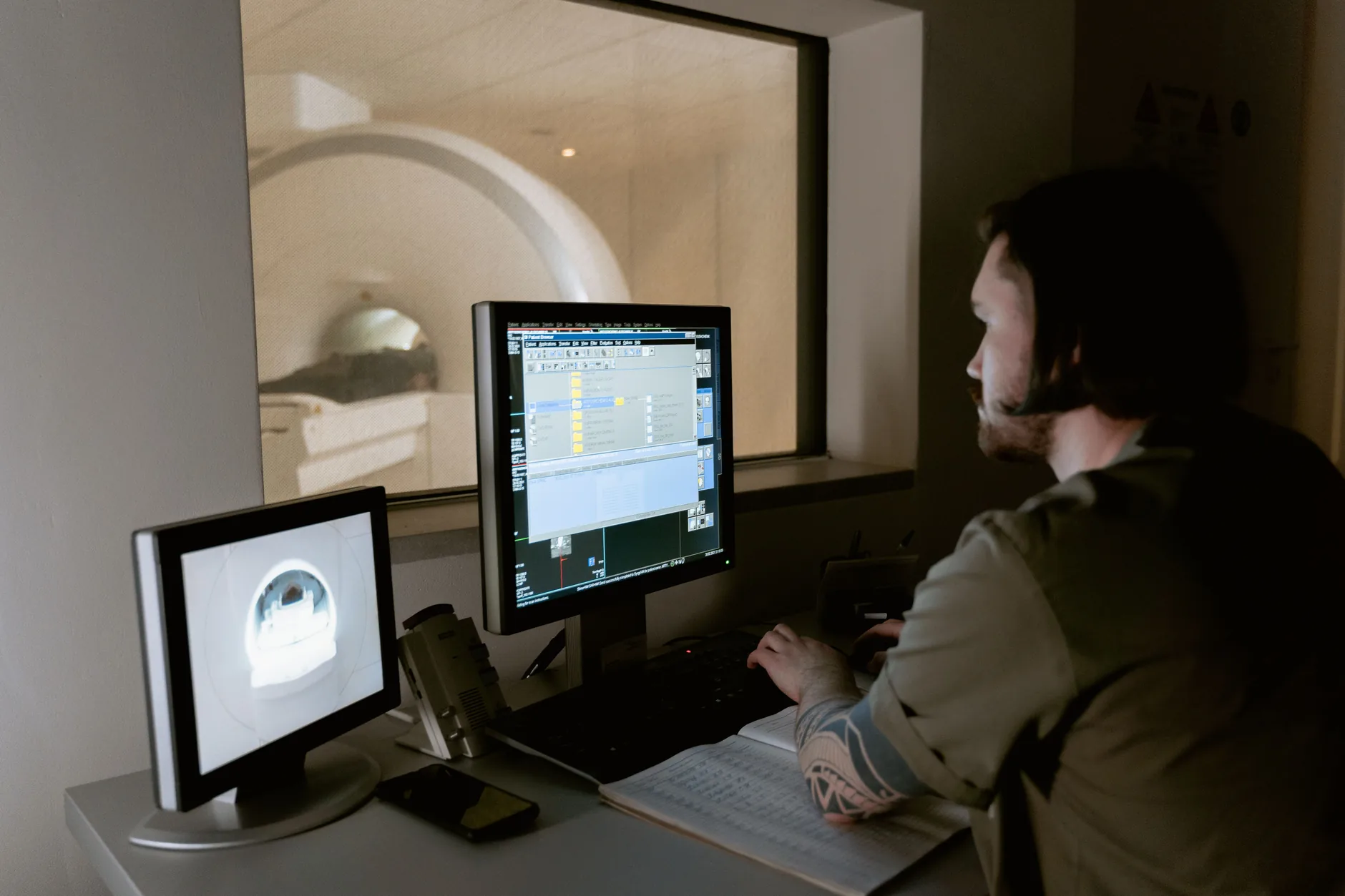 A technician reviewing MRI images on monitors in the control room next to the scanner.